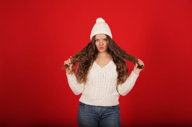 une belle jeune fille dans un chapeau d'hiver et un pull en jeans sur fond rouge