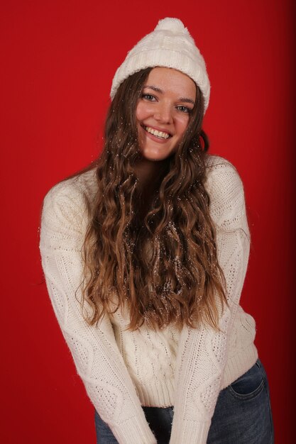 une belle jeune fille dans un chapeau d'hiver et un pull en jeans sur fond rouge