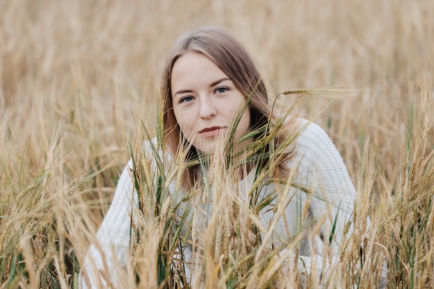 Belle jeune fille dans un pull blanc se trouve dans un champ de blé.