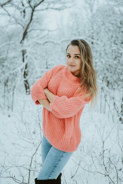 Belle jeune fille dans un pull et un jean volumineux rose dans une forêt d'hiver enneigée froide