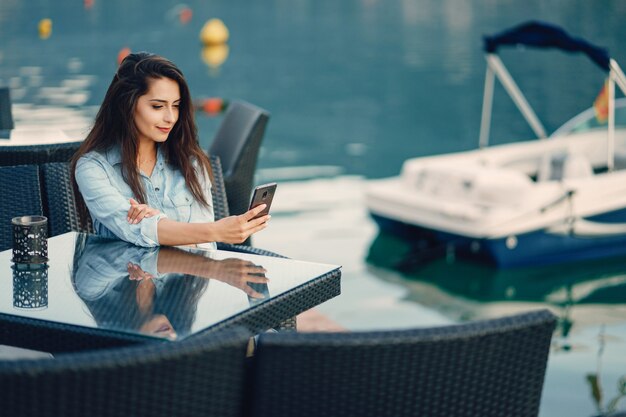 Une belle jeune fille dans une robe bleue assis près de l&#39;eau et utiliser le téléphone