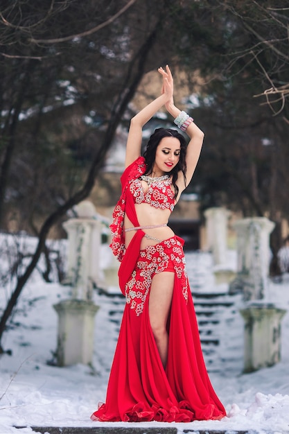 Belle jeune fille dansant la danse du ventre en robe rouge en hiver dans un parc sur la neige.