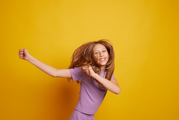 Une belle jeune fille danse en riant et s'amuse sur un fond jaune propre