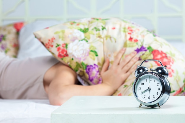 La belle jeune fille dormant dans son lit. Le service d'horloge est au premier plan