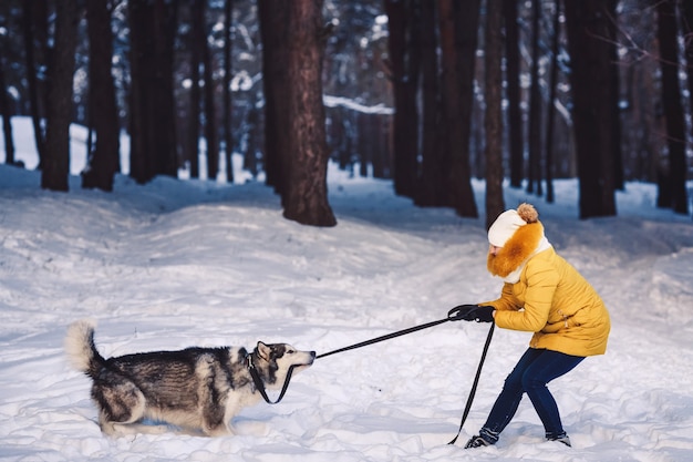 Belle jeune fille drôle jouant avec son chien en hiver dans le parc. chien et fille traînent la laisse. Concept de vacances d'hiver heureux