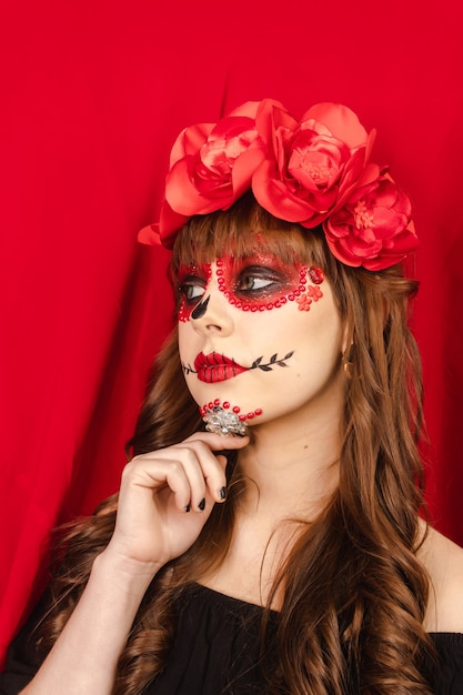 Belle jeune fille avec du maquillage Dia de los Muertos à gauche avec fond rouge.