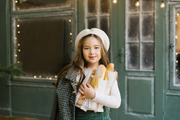 Belle jeune fille édentée de six ans souriante dans un béret blanc tenant des sacs de baguettes