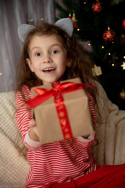 Une belle jeune fille est assise sur le canapé avec le cadeau Noël Nouvel An