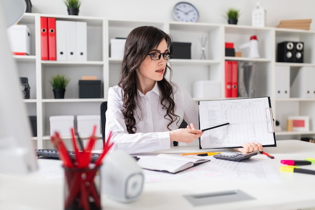 Une belle jeune fille est assise à une table dans le bureau et pointe un crayon sur les informations contenues dans le document.