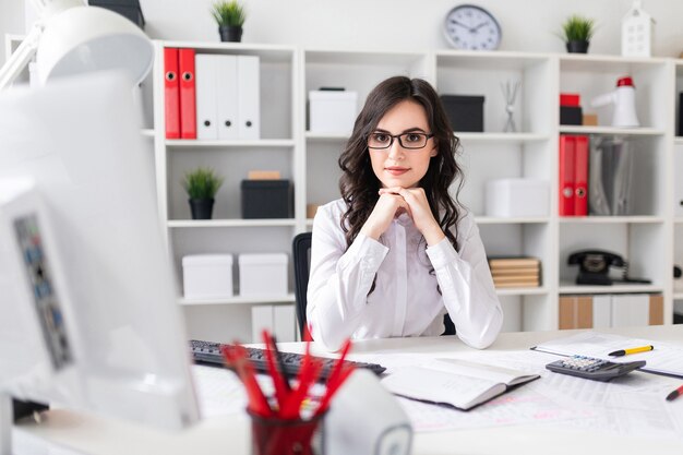 Belle jeune fille est assise à la table dans le bureau.