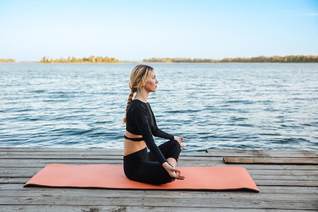 Une belle jeune fille fait du yoga dans une soirée calme et chaude sur les rives de la rivière