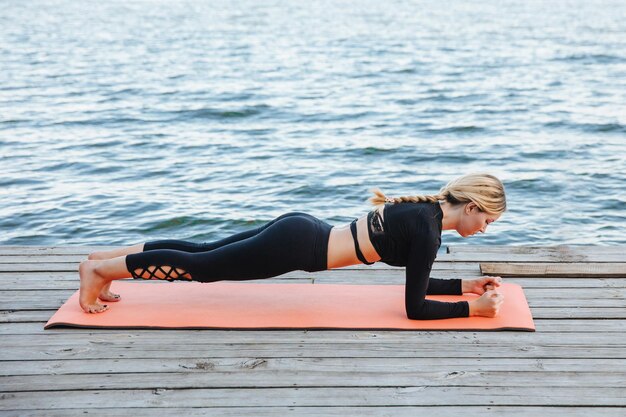 Une belle jeune fille fait du yoga dans une soirée chaude et calme sur les rives de la rivière