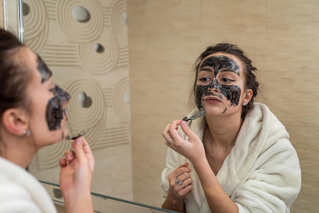 Belle jeune fille fait un masque noir pour l'acné sur le visage. Concept de masque d'acné