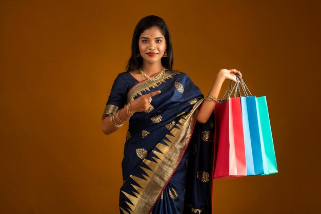 Belle jeune fille ou femme indienne tenant et posant avec des sacs à provisions sur fond marron