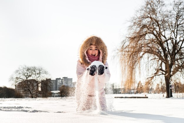 Belle jeune fille heureuse en riant portant chapeau d'hiver, écharpe recouverte de flocons de neige. Mode de vie actif. Fond de paysage de forêt d'hiver.