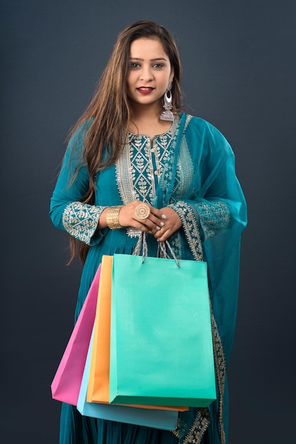 Belle jeune fille indienne tenant et posant avec des sacs à provisions sur fond gris