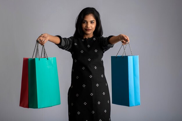 Belle jeune fille indienne tenant et posant avec des sacs à provisions sur fond gris