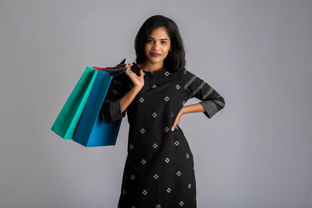 Belle jeune fille indienne tenant et posant avec des sacs à provisions sur fond gris