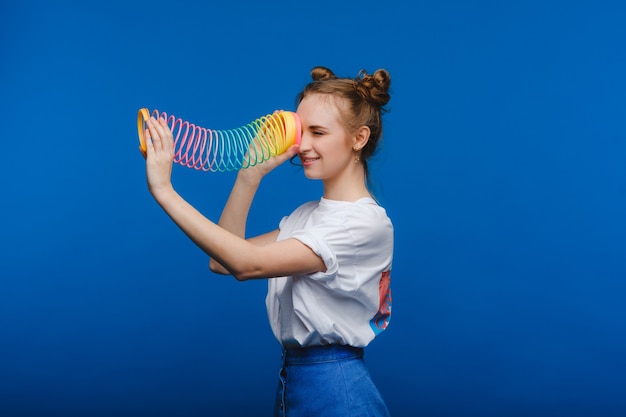 Belle jeune fille jouant avec un arc-en-ciel slinky, un jouet de son enfance sur fond bleu.