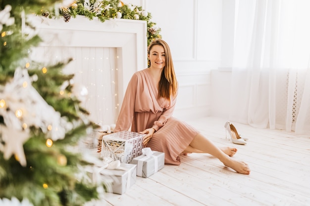 Belle jeune fille joyeuse et heureuse avec des cadeaux de Noël sur le fond d'un arbre du nouvel an à la maison