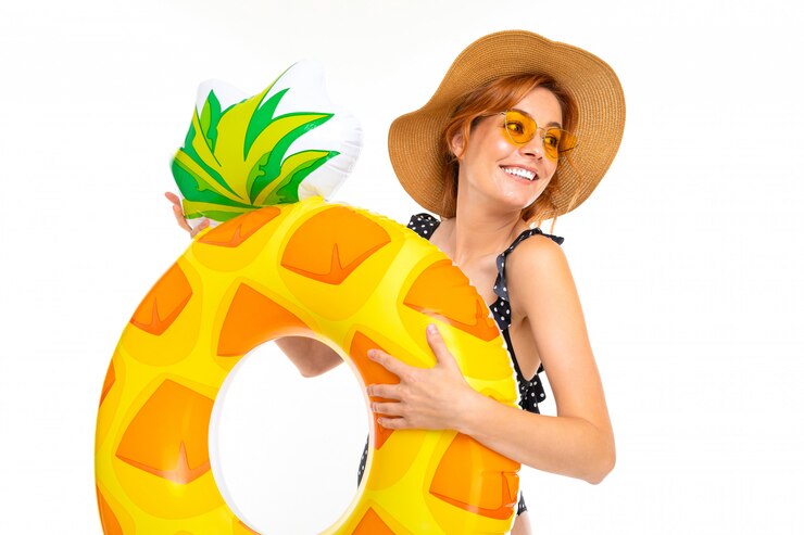 Belle jeune fille à lunettes et un chapeau de paille avec un cercle de natation en forme d'ananas sur un mur blanc