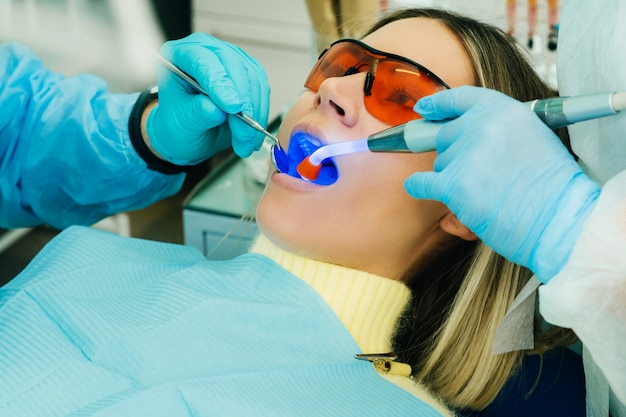 Une belle jeune fille à lunettes dentaires traite ses dents chez le dentiste avec une lumière ultraviolette. remplissage des dents.