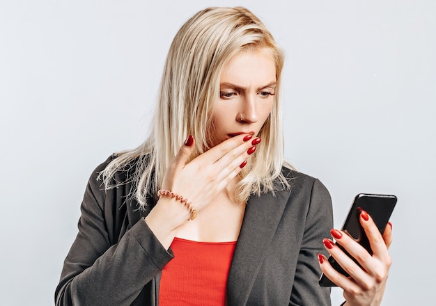 Belle jeune fille malheureuse et tenant le téléphone sur un espace isolé gris