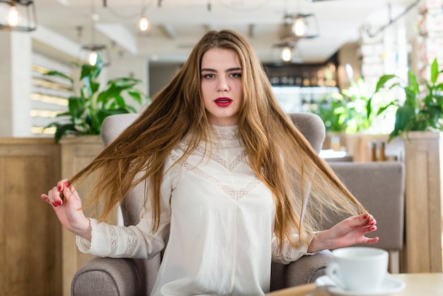 Belle jeune fille avec maquillage professionnel et coiffure assise dans un restaurant.