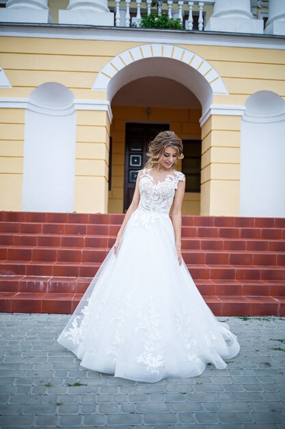 Belle Jeune Fille Mariée En Robe Blanche Avec Un Train Marchant Sur Le Fond D'une Grande Maison Avec Des Colonnes Le Jour De Leur Mariage