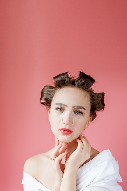 Belle jeune fille avec un masque et des bigoudis touchant son visage