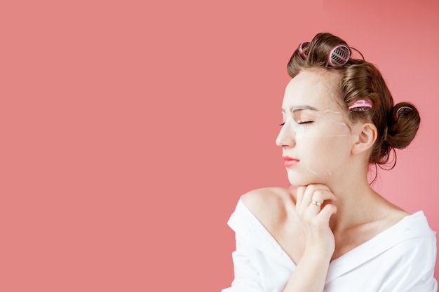 Belle jeune fille avec un masque et des bigoudis touchant son visage