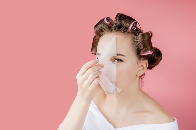 Belle jeune fille avec un masque et des bigoudis touchant son visage.