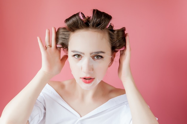 Belle jeune fille avec un masque et des bigoudis touchant son visage.