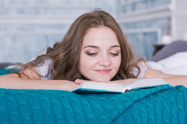 Belle jeune fille le matin au lit avec un livre dans la chambre