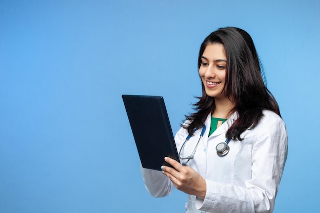 Belle jeune fille médecin asiatique, avec un ordinateur portable pour les dossiers isolés sur fond bleu. Médecin généraliste étudiant en médecine. Le concept de l'enseignement médical en Inde