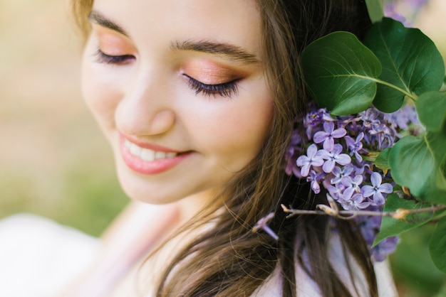 Belle jeune fille mignonne avec un maquillage professionnel se bouchent et éblouissant sourire blanc avec des fleurs lilas heureux
