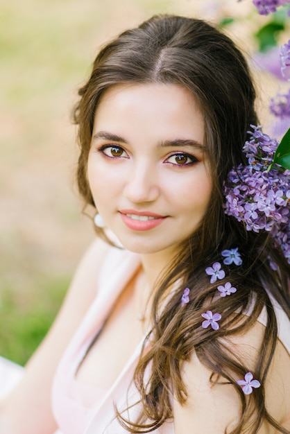 Photo belle jeune fille mignonne avec un maquillage professionnel se bouchent et éblouissant sourire blanc avec des fleurs lilas heureux