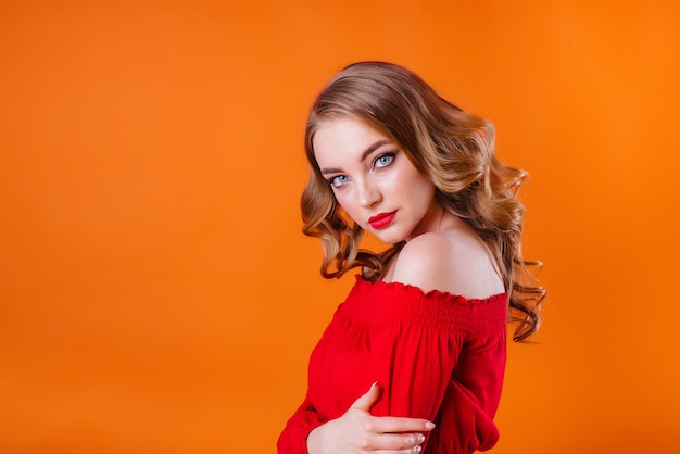 Une belle jeune fille montre des émotions et des sourires dans le Studio sur fond orange. Les filles pour la publicité.