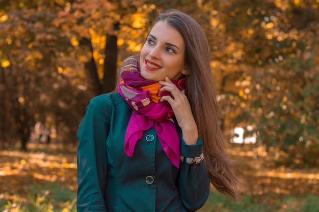 Belle jeune fille avec un mouchoir rose autour du cou se tient dans le parc et sourit