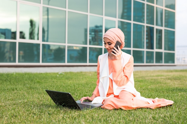 Belle jeune fille musulmane assise avec un ordinateur portable en plein air