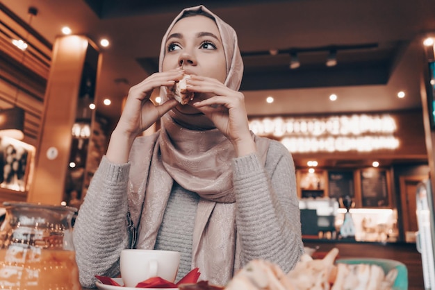 Belle jeune fille musulmane avec un foulard sur la tête en train de manger de la nourriture savoureuse dans un restaurant oriental