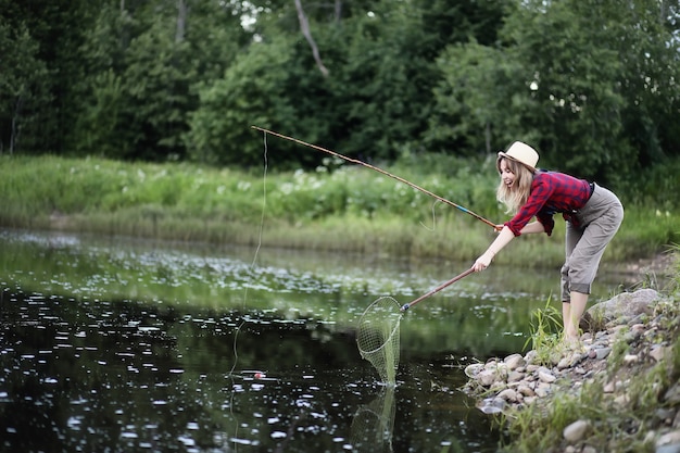 Belle jeune fille sur la nature au bord de la rivière avec une canne à pêche