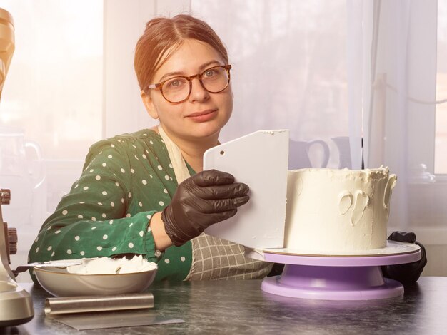 Belle jeune fille pâtissière fait un gâteau à la crème blanche à l'aide d'une spatule de cuisson