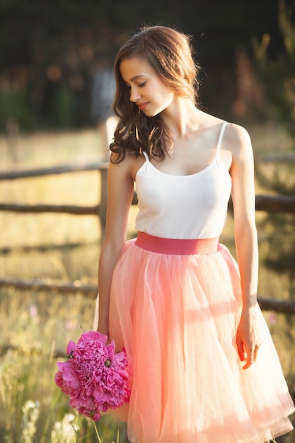 Belle jeune fille avec des pions sur la nature en plein air au soleil. Jolie femme à l'extérieur avec des fleurs dans la jupe rose