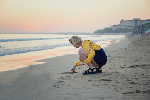 Belle jeune fille sur la plage le soir s'appuie sur le sable