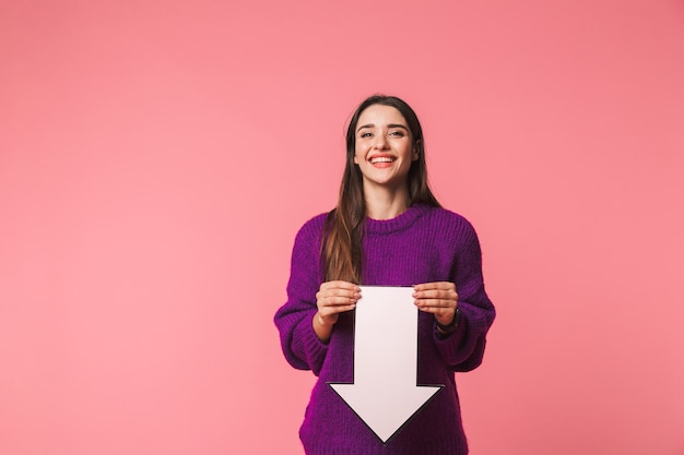 Belle jeune fille portant un chandail debout isolé sur rose, pointant avec une flèche vers le bas à l'espace de copie