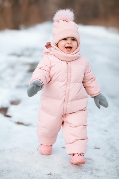 Une belle jeune fille portant une combinaison rose en cours d'exécution dans un parc d'hiver enneigé