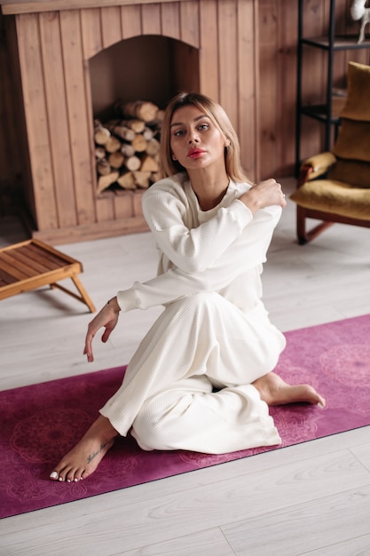 Belle jeune fille portant des vêtements de sport en coton blanc écologique naturel, assise sur un tapis dans un intérieur confortable. photo de haute qualité