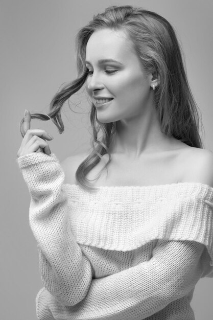 Belle jeune fille posant et assise sur fond blanc. blonde dans un pull blanc.