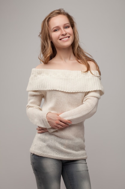 Belle jeune fille posant et souriant. blonde dans un pull blanc.